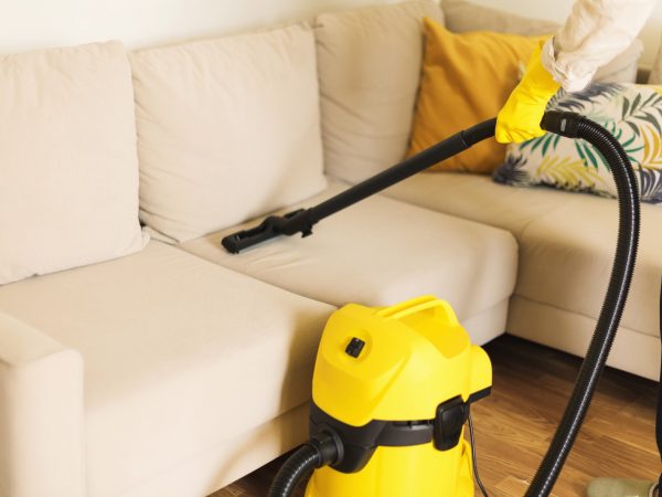 Woman cleaning sofa with yellow vacuum cleaner. Copy space. Clean concept Woman cleaning sofa with yellow vacuum cleaner. Copy space. Clean concept
